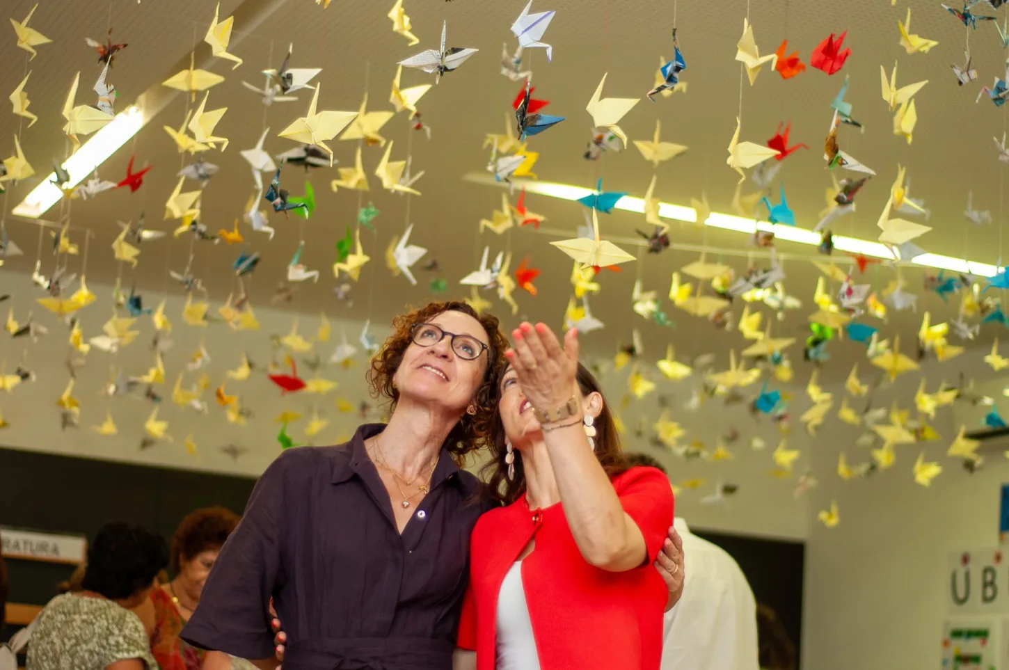 Duas mulheres a olhar para centenas de grous de papel suspensos no teto, no Seminário Educar Hoje